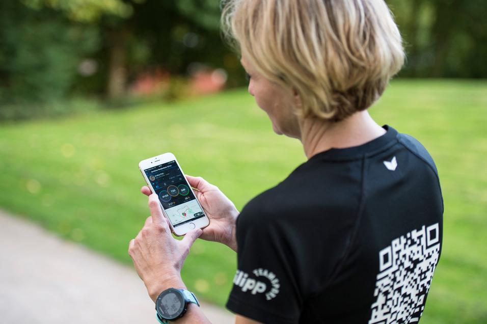 Frau mit kurzen Haaren schaut auf ein Smartphone, während sie auf einem Weg in einem Park steht.